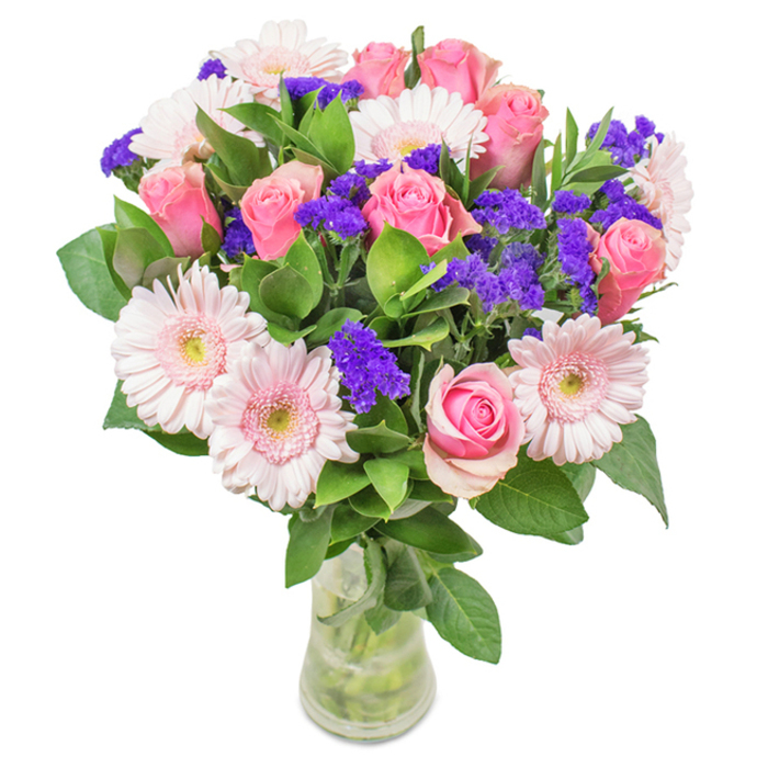 A sophisticated and vibrant Temple-inspired bouquet sits gracefully in a transparent glass vase, placed against a bright white backdrop reminiscent of the district's historic architecture. The centerpiece is formed by 7-9 sumptuous pink roses, some still tightly closed, while others are beginning to reveal their signature spiral form-each petal velvety and delicately tinted. Complementing these are 5-7 pale pink gerbera daisies, their broad, generously layered petals and nearly white centers offering a fresh, contemporary touch. Nestled throughout the arrangement, clusters of striking purple statice add texture and depth, their hue a bold contrast to the pastel blooms. Lush, dark green foliage-reflective of the verdant Temple Church gardens-spills between the blossoms, supporting each and lending a sense of wild abundance. The clean lines of the clear vase, filled with freshly cut stems and crystal water, evoke the purity and clarity of a Temple morning. Suitable for everything from birthdays to anniversaries or as an elegant feature in a Temple legal office, this arrangement brings celebration, sophistication, and heartfelt meaning into any setting.